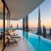 A luxurious balcony with a curved infinity pool overlooks skyscrapers, including the Burj Khalifa, at sunset in a modern cityscape. Lounge chairs sit by the pool, and glass walls reflect the urban skyline. | RealEstateMarket