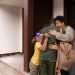 A family embraces outside a house; the child holds a small American flag, welcoming home a loved one in military uniform. | RealEstateMarket