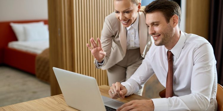 A smiling man and woman in business attire participate in a video call on a laptop. | RealEstateMarket
