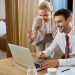 A smiling man and woman in business attire participate in a video call on a laptop. | RealEstateMarket